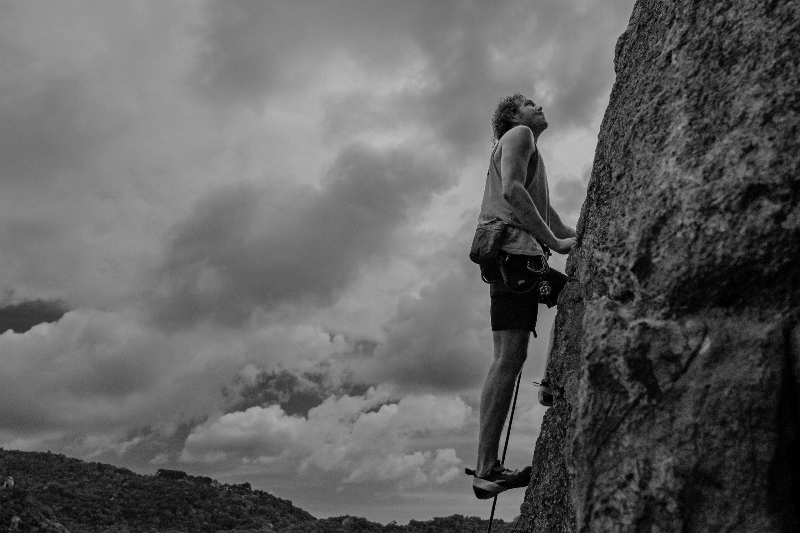 black and white photo of male climbing rocky cliff
